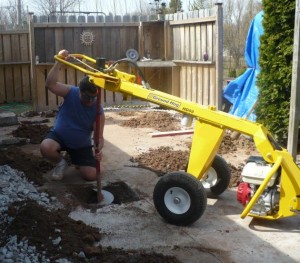 worker shown using ground hog post hole digger machine