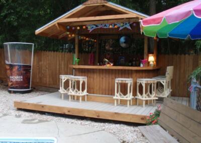 backyard tiki bar built on a deck with white bar stools